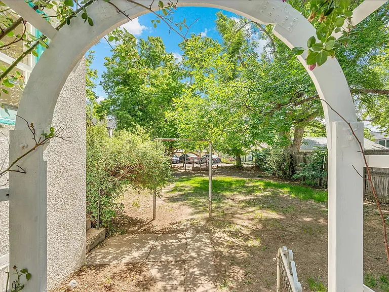 Large fenced in back yard with mature trees and an area for a patio and seating