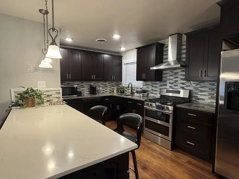 Kitchen features a large breakfast bar, dark cabinetry, mosaic tile backsplash, and stainless steel appliances.