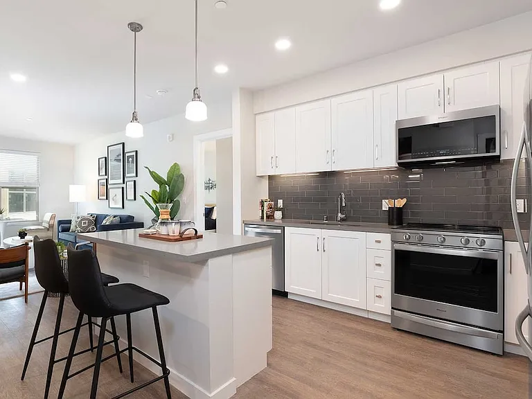 Upgrade Collection kitchen and dining area with stainless steel appliances, white cabinetry, grey quartz countertop, grey tile backsplash, and hard surface flooring