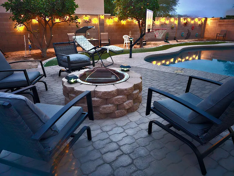 Resort-style backyard with a pool, paver patio lounge seating, fire pit, and string lights for relaxing evenings.