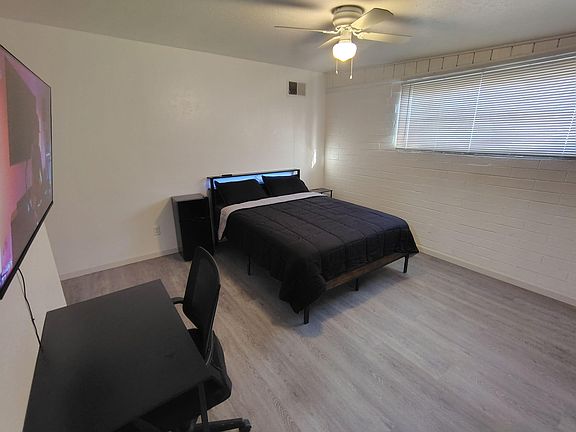 Furnished bedroom featuring a full bed with nightstand, ceiling fan, and a large window with blinds for natural light.