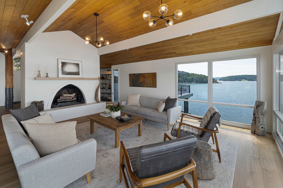 A dramatic arched fireplace anchors the elegant living room, complemented by warm wood ceilings and sweeping views across Cayou Channel.