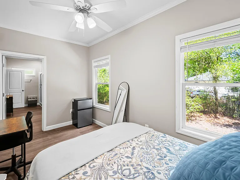 Spacious bedroom featuring large windows, ceiling fan lighting, and a dedicated desk area with convenient in-room storage.