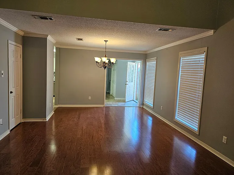 Living room & dining area with wood floors, crown molding, & large windows.
