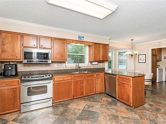Kitchen featuring wood cabinetry, stainless steel appliances, a tiled backsplash, patterned flooring, and a peninsula with countertop