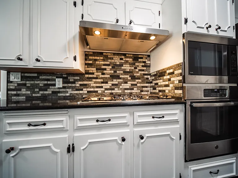 Kitchen detail with tile backsplash, stove, microwave, and countertops