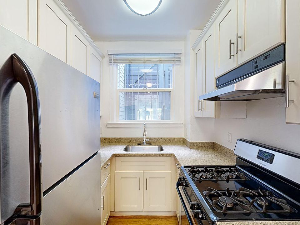 Kitchen with multiple cabinets, refrigerator, stove, range hood, and sink
