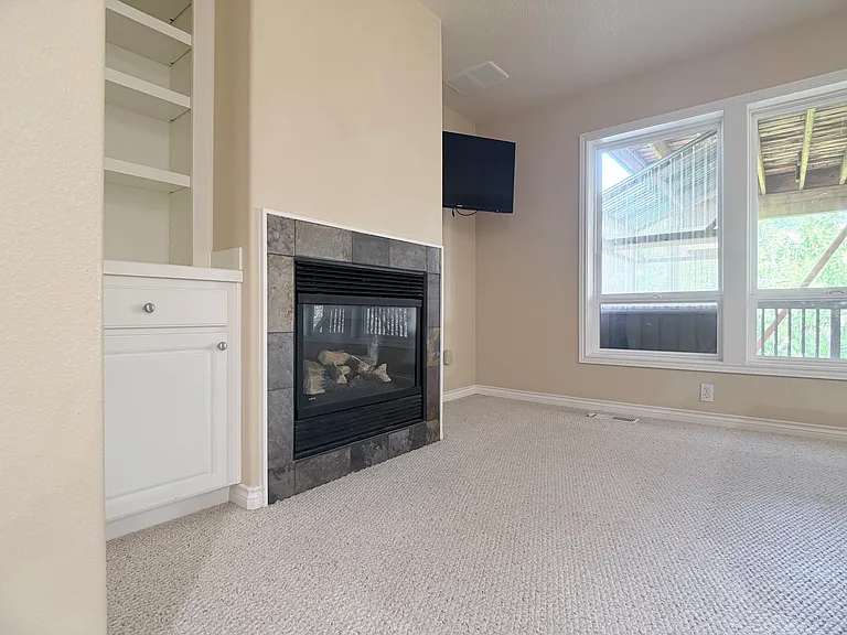 Additional view of the lower-level living space, featuring custom built-ins, a secondary bar TV, and a gas fireplace.