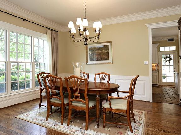 Dining room has view of front lawn, wainscot paneling, and hardwood floors.