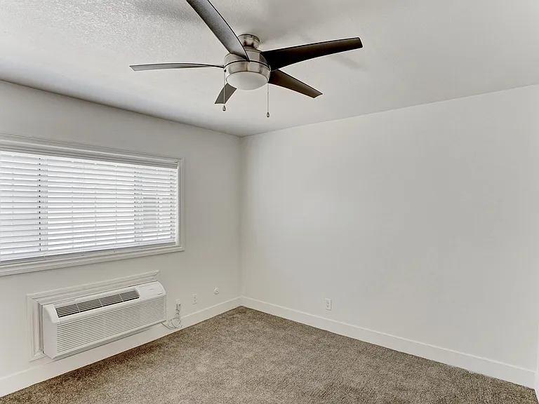 A room with a ceiling fan and a window with blinds.