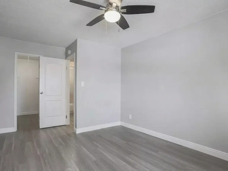 Bright and airy empty room with sleek gray flooring, a modern ceiling fan, and a white door opening to a closet space.