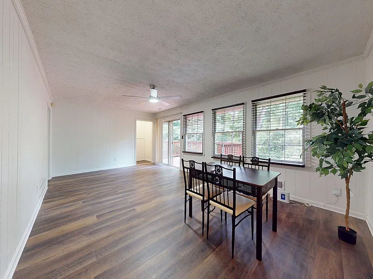 Bright dining area with wood-look floors, ceiling fan, large windows, and easy deck access.