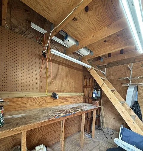 Shed interior with built in work table. Stairs leading to loft storage area are retractable, so they can be lifted out of the way when not needed.