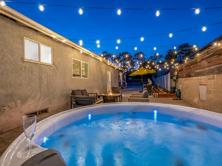 String lights elegantly drape across the patio, casting a warm glow as the sun sets into a beautiful gradient sky while you soak your cares away in the hot tub under the stars.