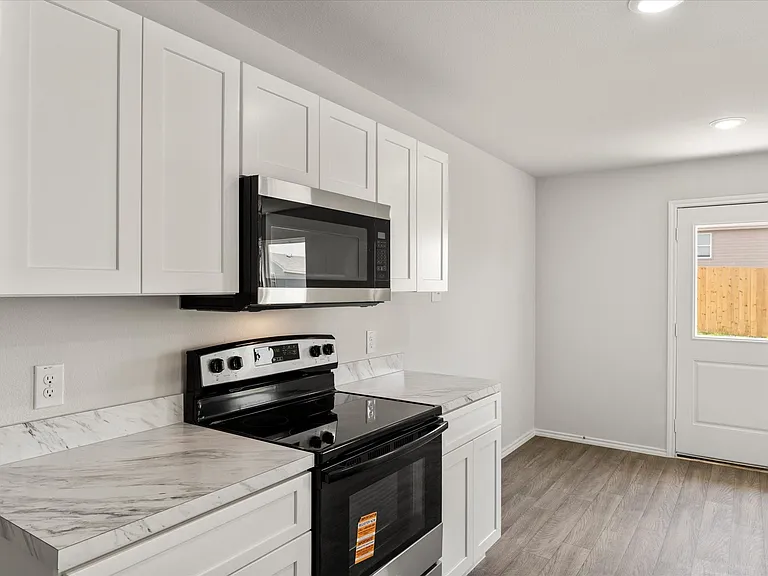 Bright kitchen featuring white shaker cabinetry, stainless steel microwave, black electric range, and light-toned countertops