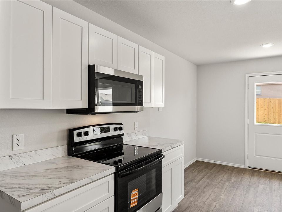 Bright kitchen featuring white shaker cabinetry, stainless steel microwave, black electric range, and light-toned countertops
