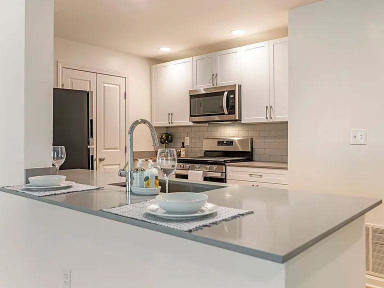 Renovated Package I kitchen with white cabinetry, grey quartz countertops, grey tile backsplash, stainless steel appliances, and hard surface plank flooring