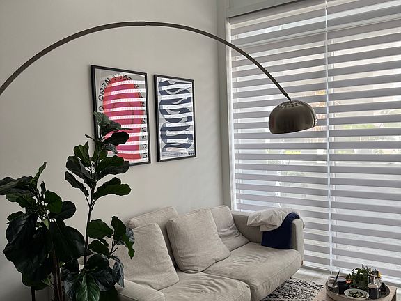 Living Area - Sun-drenched living room with expansive windows, creating a warm and inviting atmosphere. Perfect for relaxing or entertaining in a bright, airy environment. Zebra shades provide added privacy without compromising natural light exposure.