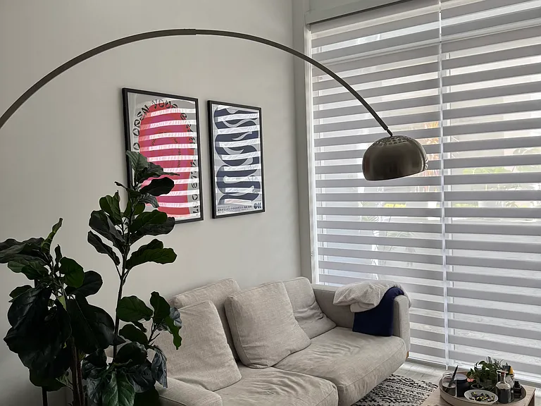 Living Area - Sun-drenched living room with expansive windows, creating a warm and inviting atmosphere. Perfect for relaxing or entertaining in a bright, airy environment. Zebra shades provide added privacy without compromising natural light exposure.