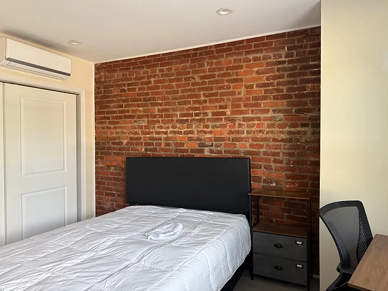Bedroom with exposed brick accent wall, bed, bedside table, and mini-split A/C for added comfort year-round.