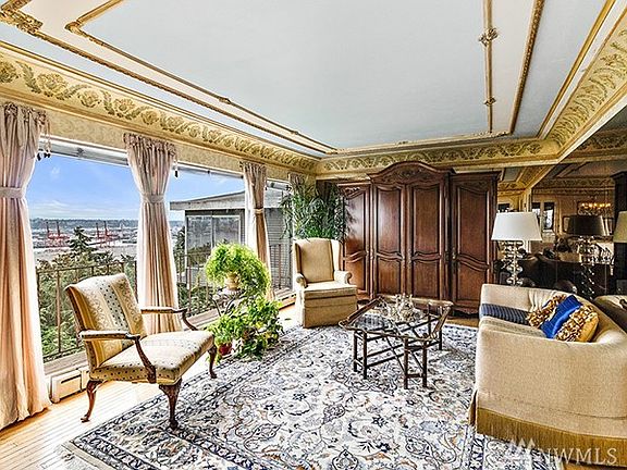 Large formal living room features ornate sculpted ceiling, Russian white oak flooring, and full-length, East-facing view windows.