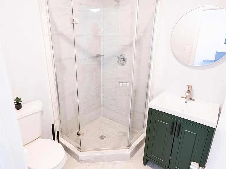 Updated bathroom with a glass corner shower, large-format tile surround, and a single-sink vanity with storage.