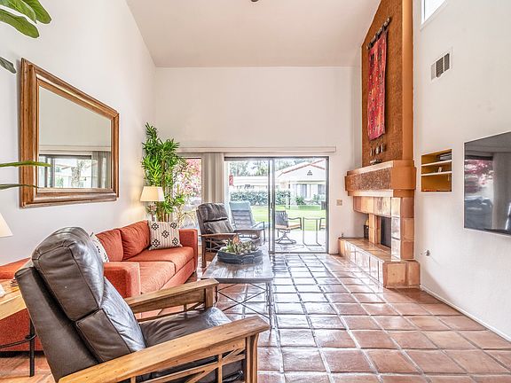 Bright and inviting living room with Saltillo tile floors, fireplace, tall ceilings, and sliding doors opening to a private greenbelt patio. Warm desert tones and multiple seating areas create a relaxed yet elevated Santa Rosa Cove retreat.