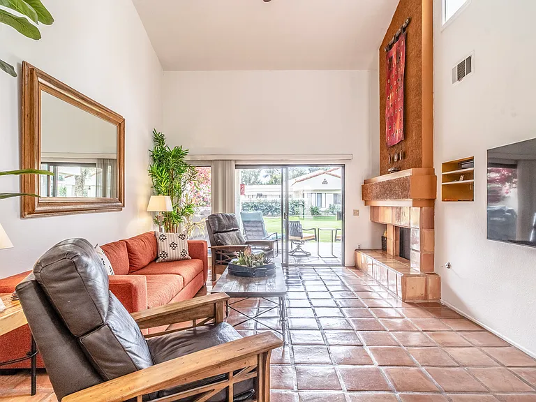 Bright and inviting living room with Saltillo tile floors, fireplace, tall ceilings, and sliding doors opening to a private greenbelt patio. Warm desert tones and multiple seating areas create a relaxed yet elevated Santa Rosa Cove retreat.