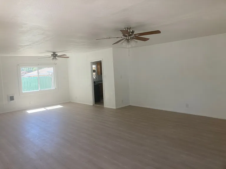 View from the southeasern corer of the large combination living room/dining room show both ceiing fans, one of the dining room windows and the door to the kitchen