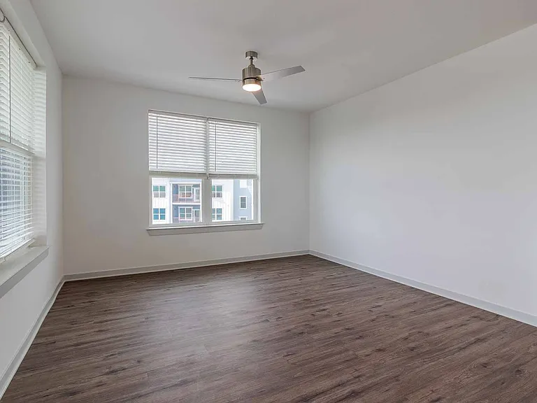 Large, bright living room with corner windows, a ceiling fan, and wood-style plank flooring Large, bright living room with corner windows, a ceiling fan, and wood-style plank flooring