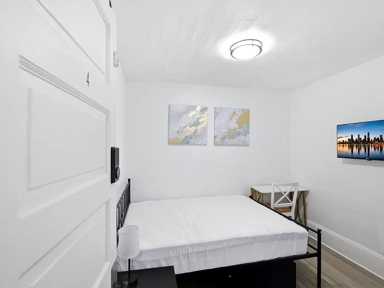Private bedroom with a full bed, wall-mounted TV, and a compact desk areaideal for sleep, study, and streaming.