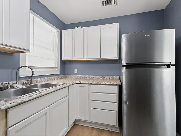 Efficient kitchen with ample cabinet storage, laminate-style counters, double-basin sink, and a full-size refrigerator.