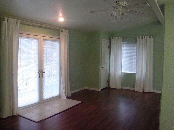 French doors open to large living room with laminate floor, ceiling fan and large windows.