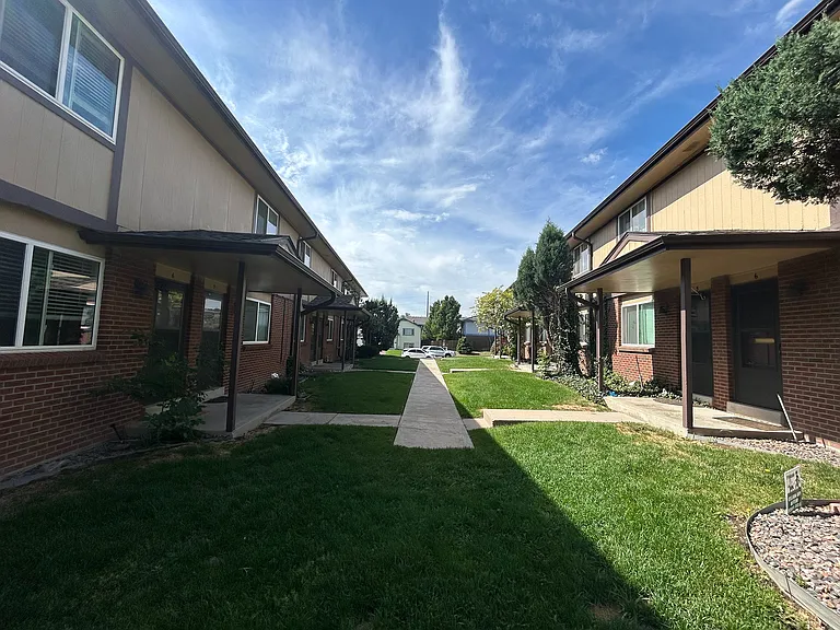 Charming suburban apartment complex with lush green lawns and elegant brick exterior under a clear blue sky.