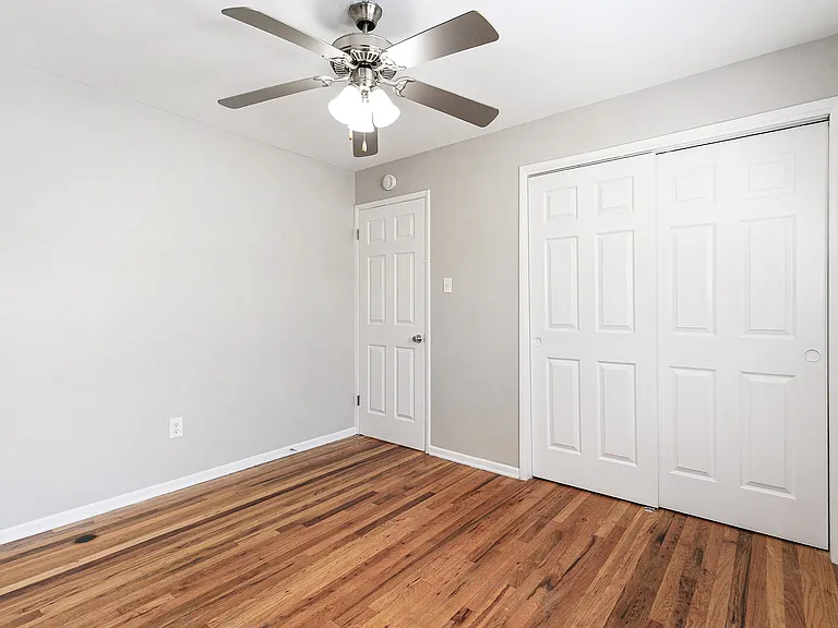 Bright and inviting room featuring elegant hardwood floors, a sleek ceiling fan, and spacious white double closet doors.