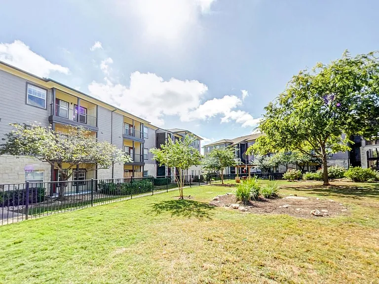 Fenced in dog park with large green space and shade trees
