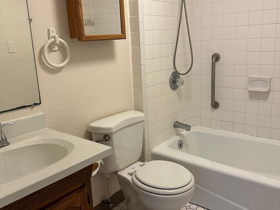 Bathroom with vanity and large mirror plus medicine cabinet. Full tile-surround on tub. Hand-held shower. Tile floor.