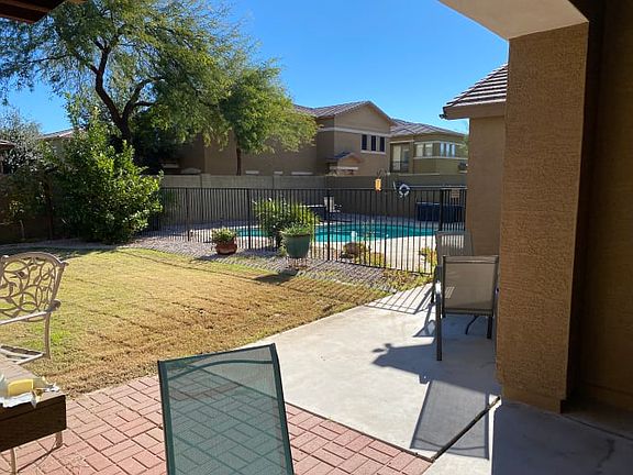 Backyard viw of pool from patio with chairs and grass. Grass is removed with gravel in place