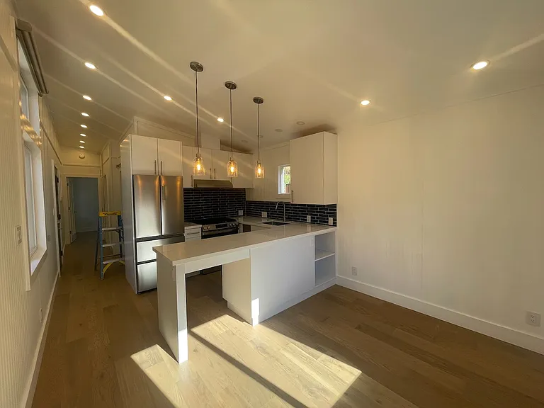 Open concept chef's kitchen/living room with high ceilings and natural light.