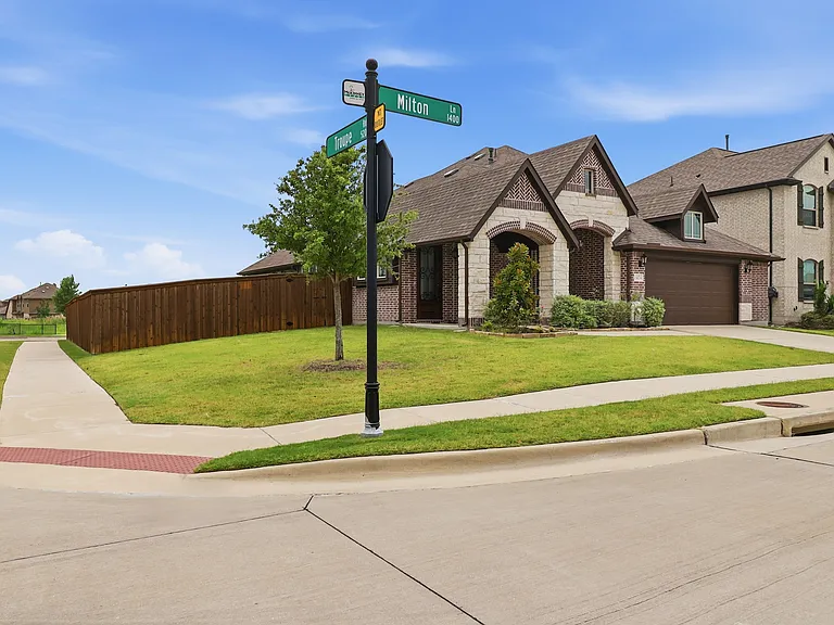 Corner lot residence featuring a brick and stone facade, arched entryway, and a two-car garage with a brown door