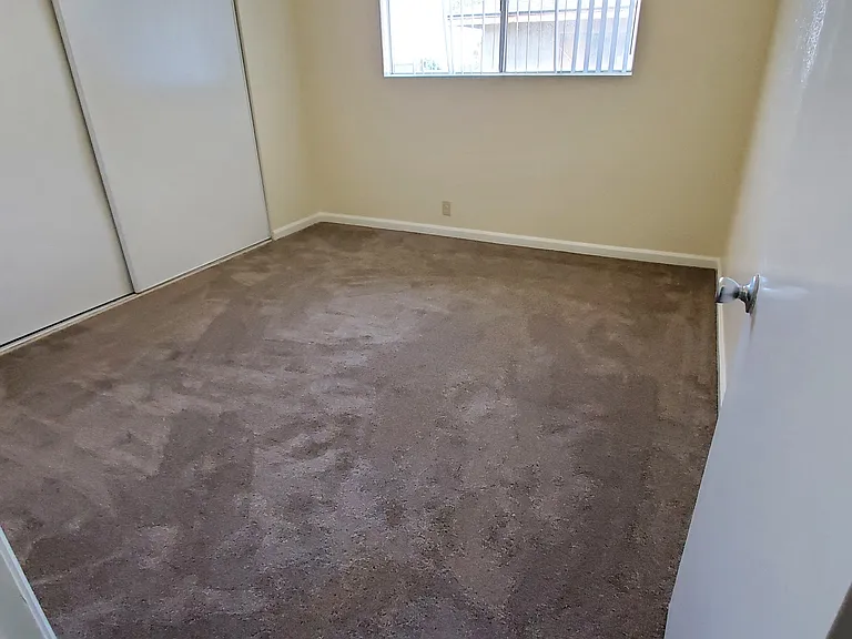 Carpeted bedroom with large closets and window at Zenith Place Apartments in Chula Vista, California.
