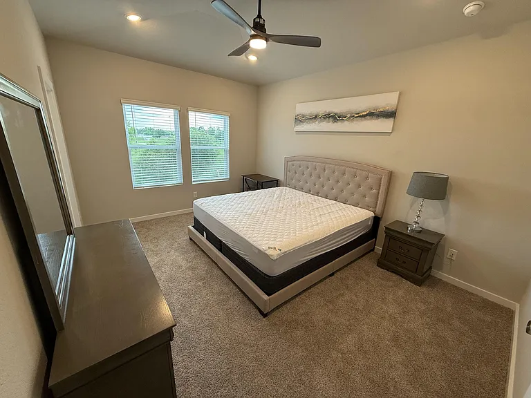Spacious bedroom with a large window, ceiling fan, and ample space for a full furniture setup and storage.