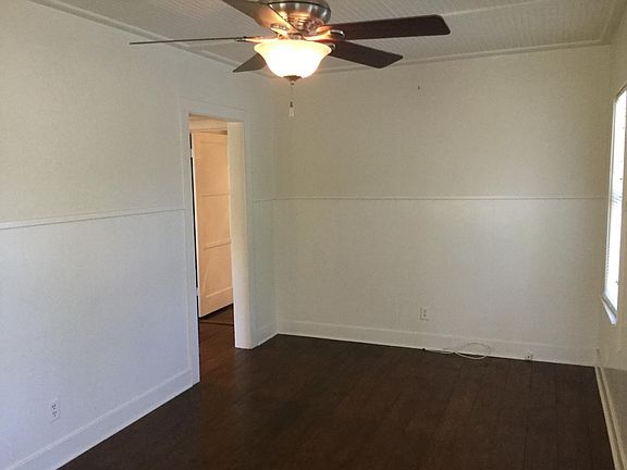 Living area has ceiling fan with light, wood floors, blinds in windows.