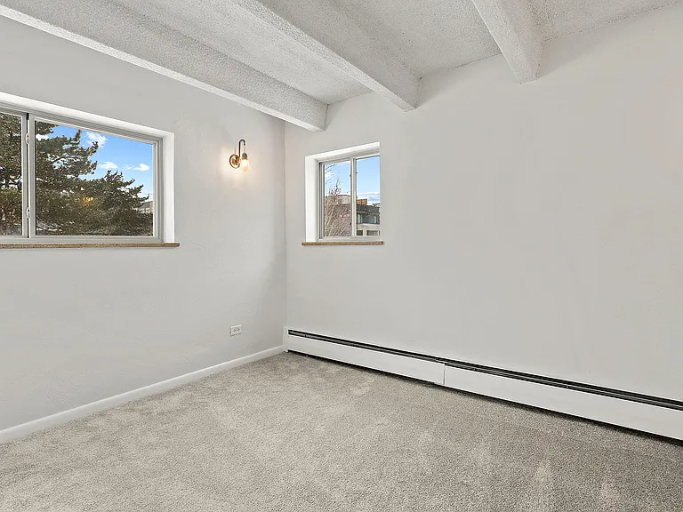 Bright, minimalist room with plush carpet, two large windows, and stylish wall light, offering a cozy and inviting atmosphere.