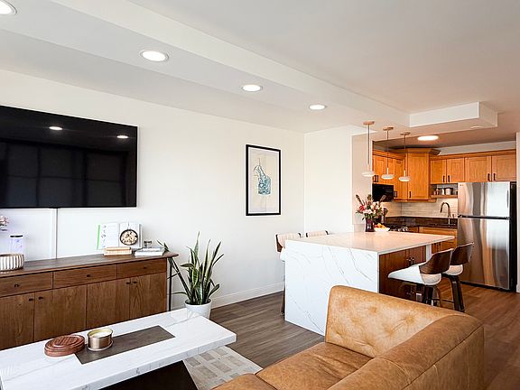 View of living area and kitchen. 65" Smart TV. Cable channels available with internet service.