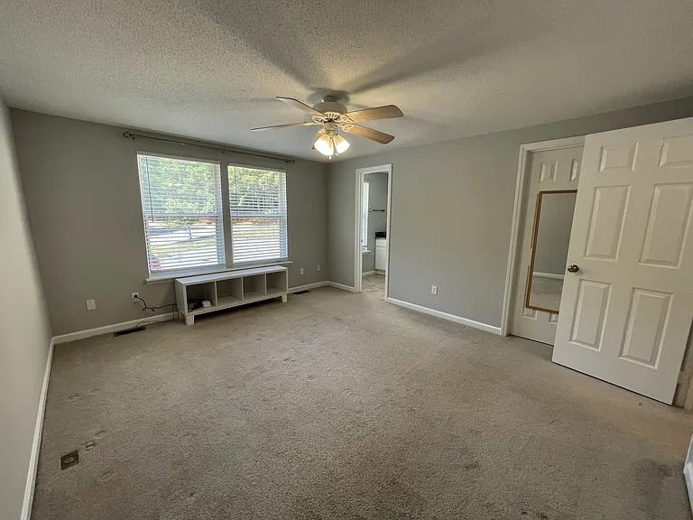 Main bedroom with en suite bathroom, custom under-window storage, ceiling fan, and walk-in closet