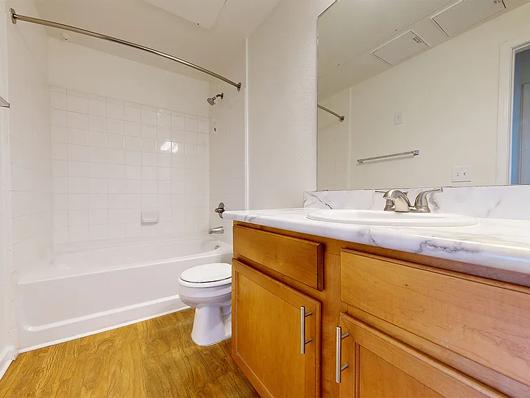 Apartment bathroom with wood-style flooring and marble-style countertops (shown here). Quartz-style countertops are available in select homes.