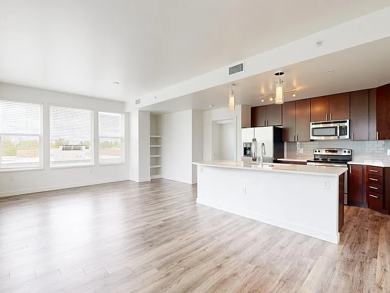 Apartment kitchen with stainless steel appliances, dining and living room with wood-style flooring.