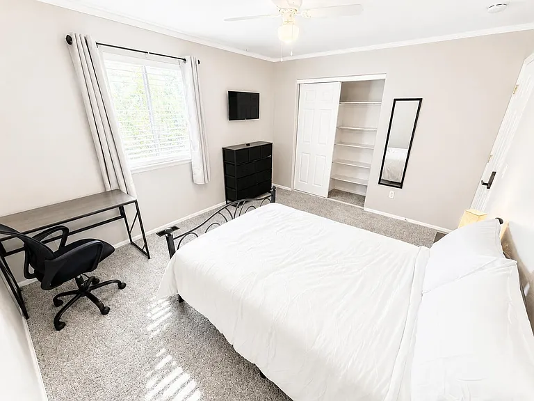 Private bedroom with a bed, work desk, and dresser, plus a closet with built-in shelving and a wall-mounted TV.