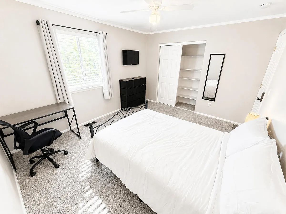 Private bedroom with a bed, work desk, and dresser, plus a closet with built-in shelving and a wall-mounted TV. - Dexter St